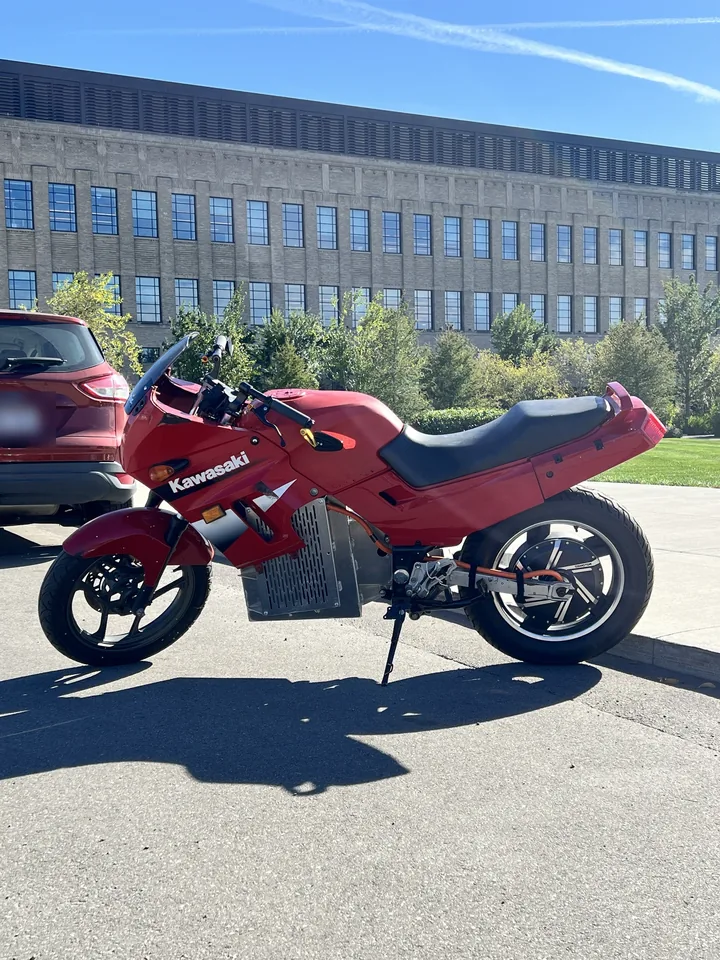Kawasaki Ninja 250 eléctrica roja de perfil: paquete de baterías ventilado bajo el carenado y motor de buje trasero.