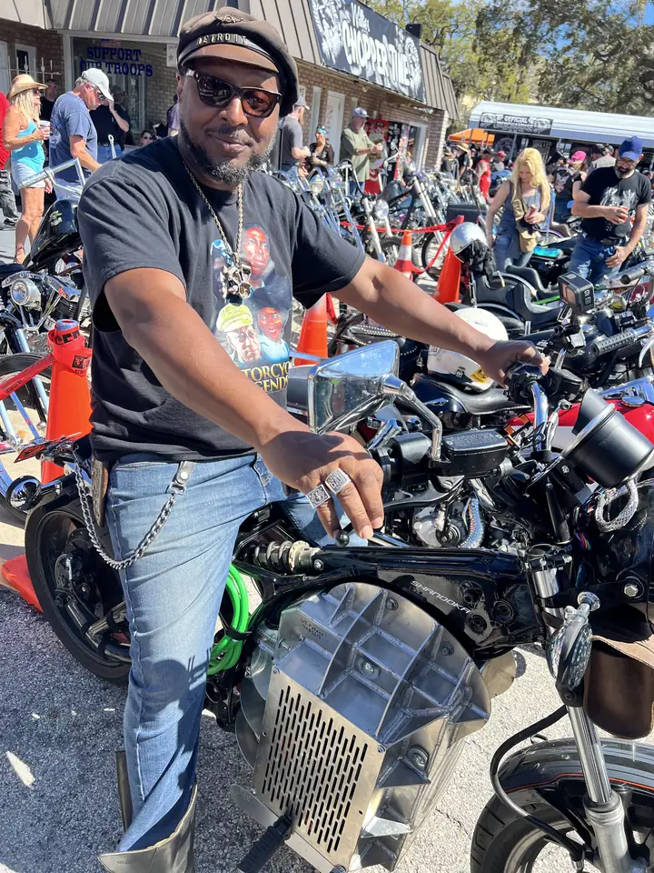 Una persona maniobrando una conversión eléctrica Shandoka en un rally lleno de gente, con otras motos estacionadas atrás.